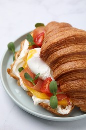 Tasty croissant with fried egg, tomato and microgreens on white table, closeup