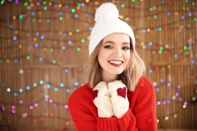 Beautiful young woman in warm clothes posing on blurred lights background. Christmas celebration
