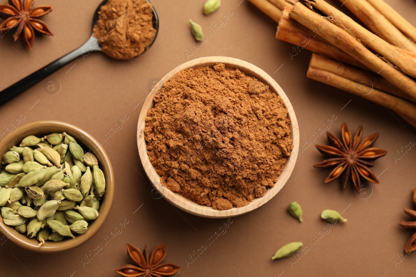 Photo of Cinnamon sticks, powder, star anise and cardamom pods on brown background, flat lay