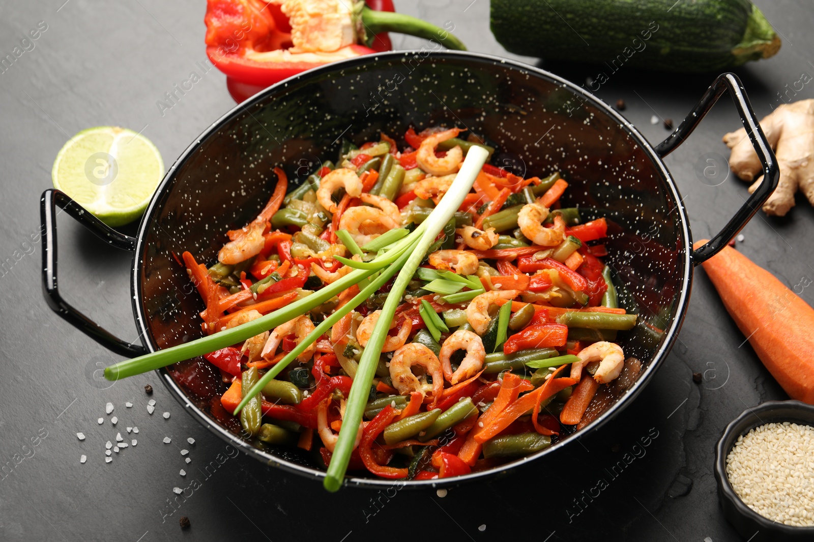 Photo of Shrimp stir fry with vegetables in wok and ingredients on black table