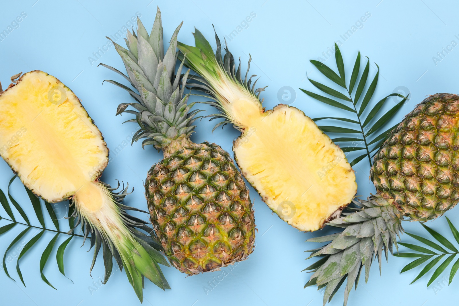 Photo of Whole and cut ripe pineapples on light blue background, flat lay