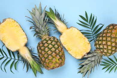 Whole and cut ripe pineapples on light blue background, flat lay