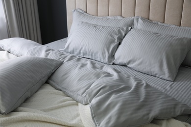 Photo of Comfortable bed with soft blanket and pillows indoors, closeup