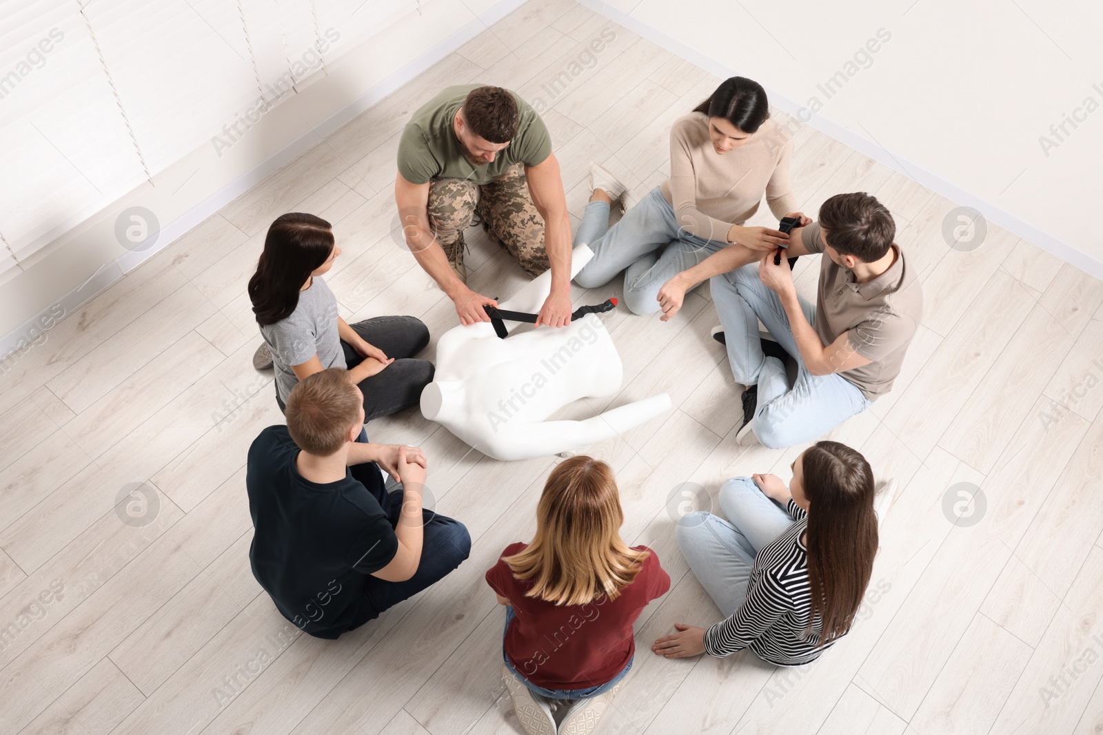 Photo of Soldier in military uniform teaching group of people how to apply medical tourniquet indoors, above view