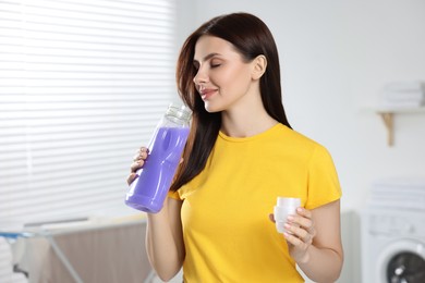 Woman smelling fabric softener in bathroom, space for text