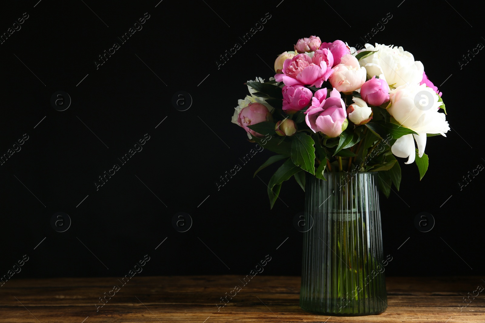 Photo of Bouquet of beautiful peonies in vase on wooden table against black background. Space for text