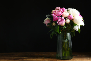 Photo of Bouquet of beautiful peonies in vase on wooden table against black background. Space for text