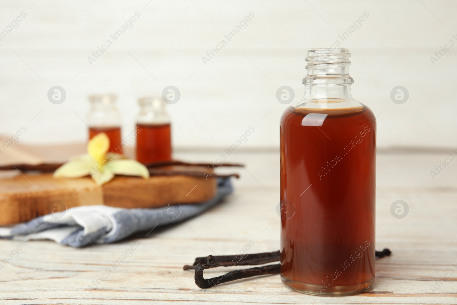 Photo of Aromatic homemade vanilla extract on white wooden table. Space for text