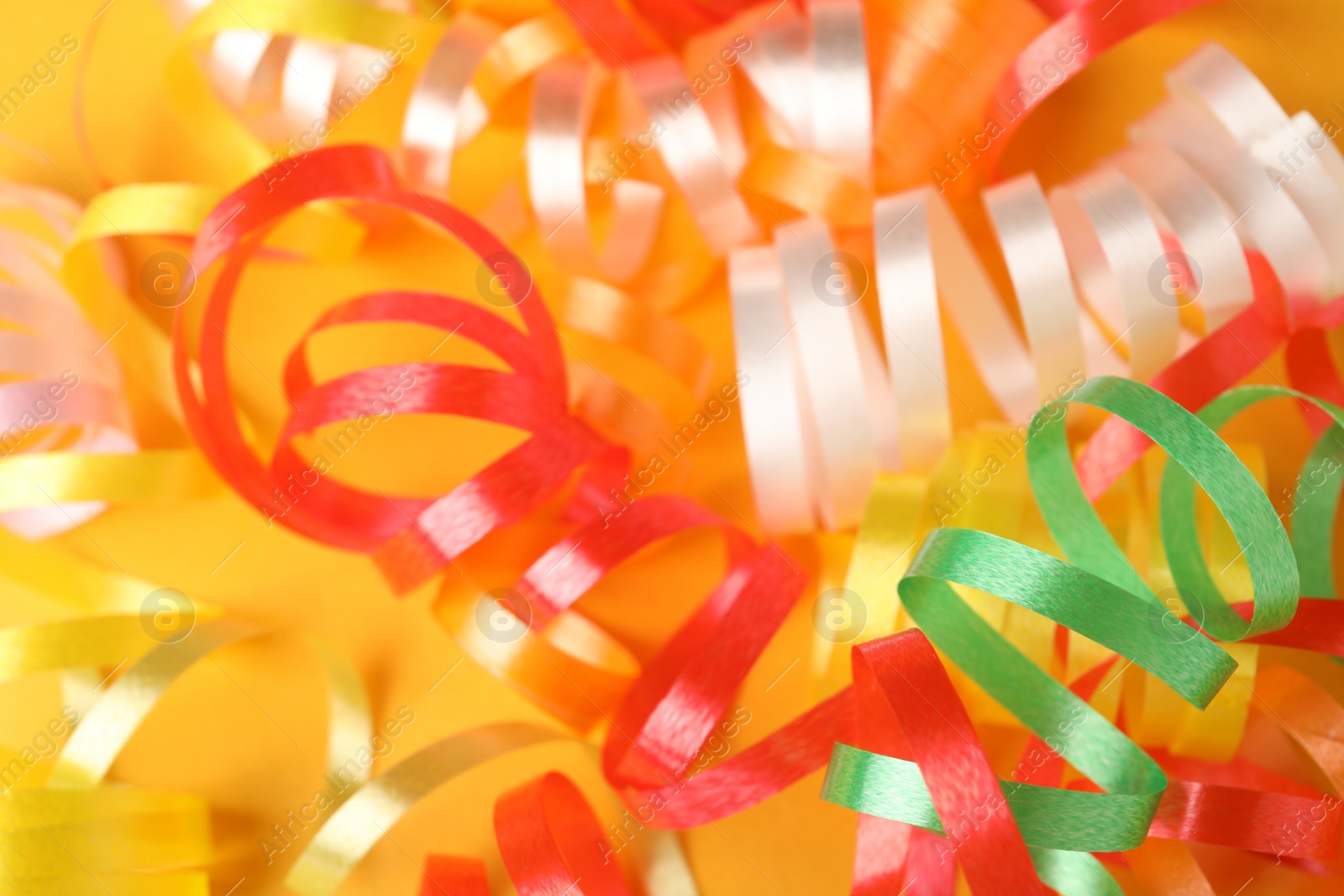 Photo of Colorful serpentine streamers on yellow background, closeup