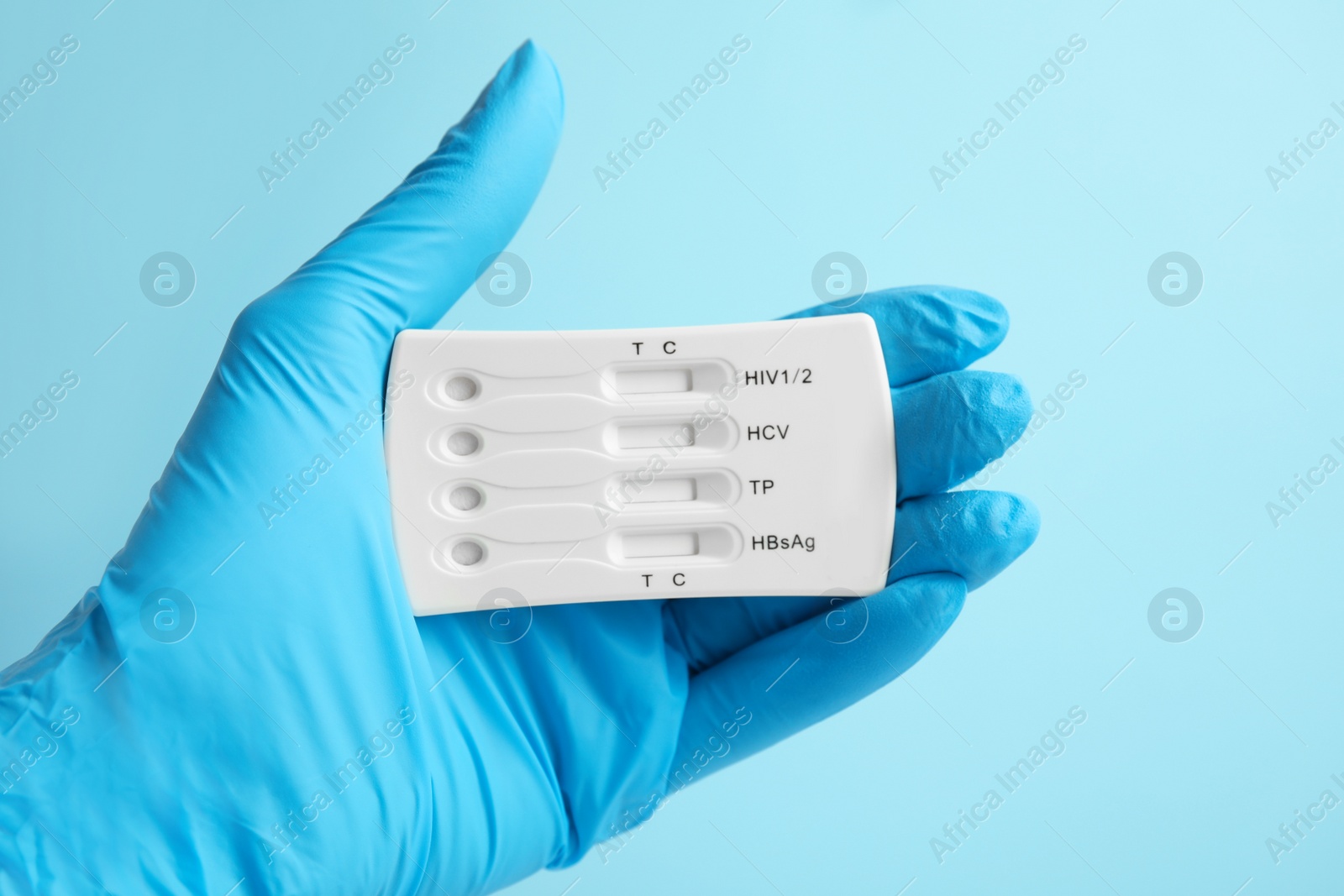 Photo of Doctor holding disposable express test for hepatitis on light blue background, closeup