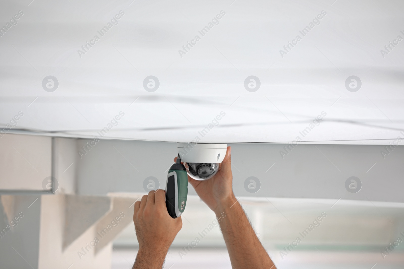 Photo of Technician installing CCTV camera on ceiling indoors, closeup