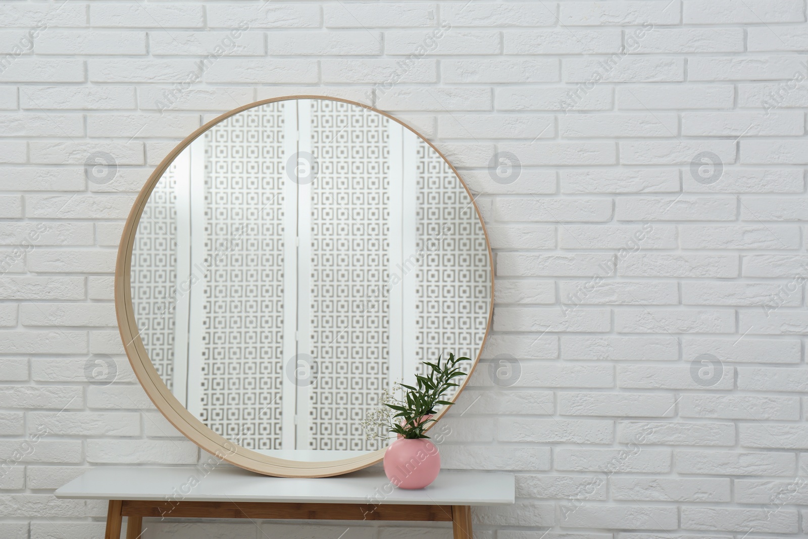 Photo of Round mirror and green plant near white brick wall