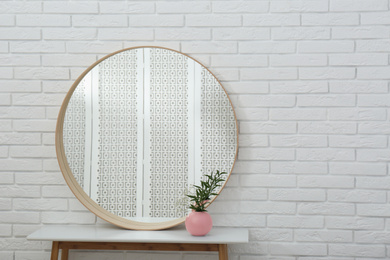 Round mirror and green plant near white brick wall