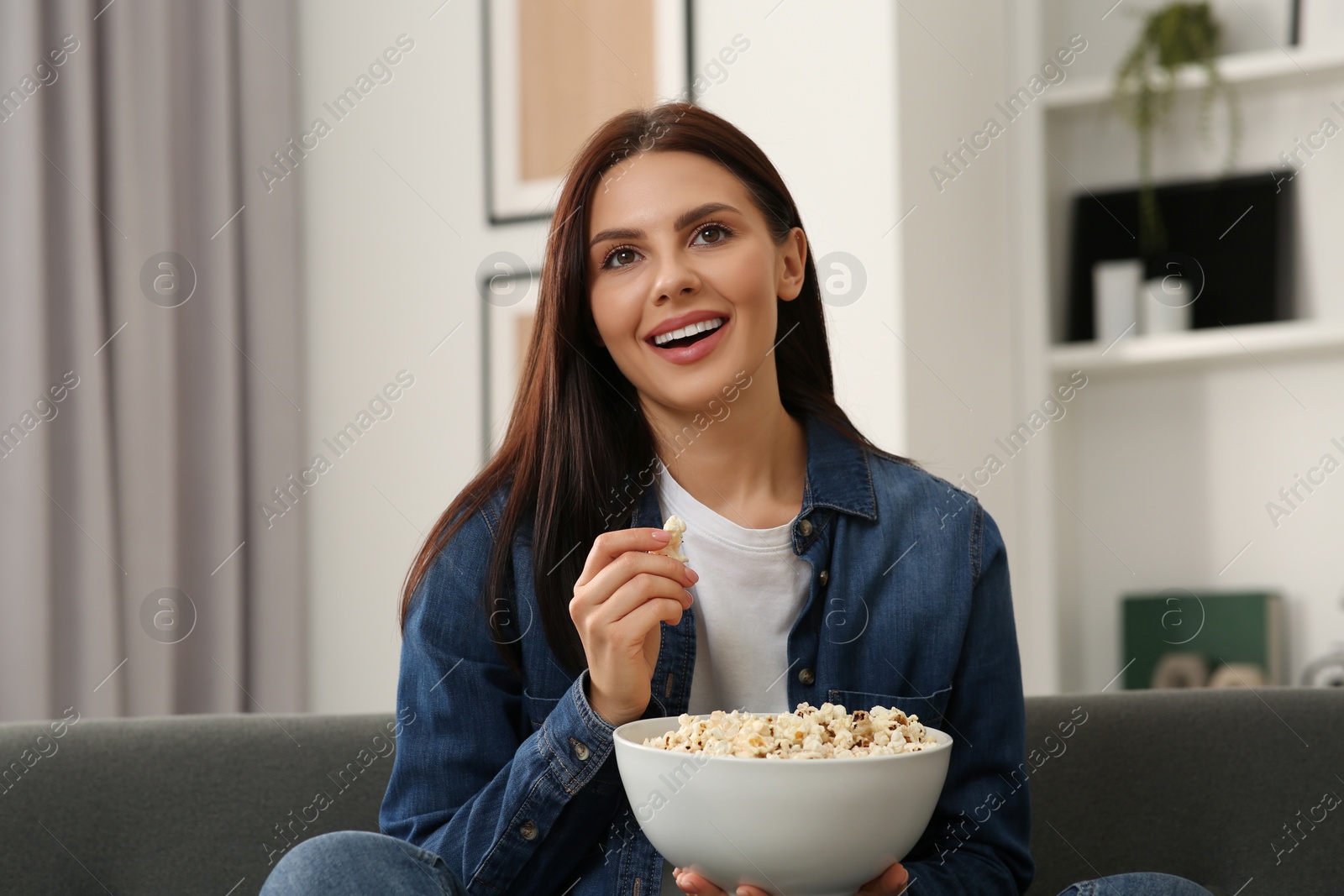 Photo of Happy woman with bowl of popcorn watching TV at home