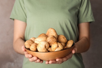 Woman holding bowl with dried figs on color background, closeup. Healthy fruit