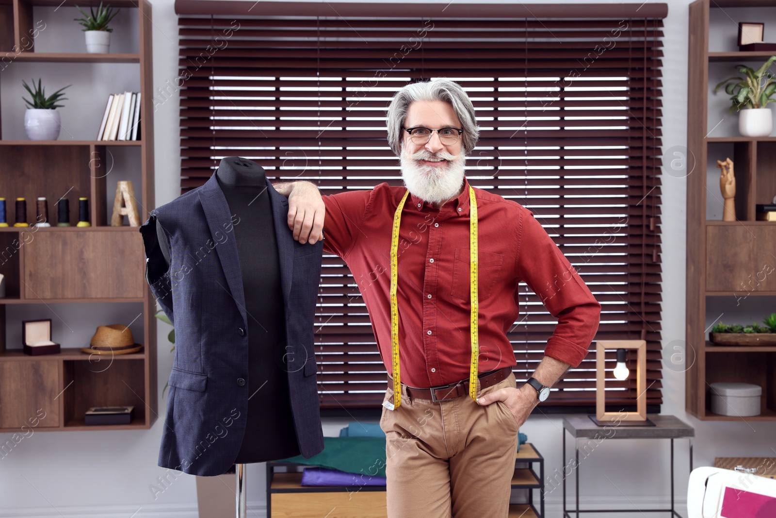 Photo of Professional tailor with measuring tape near mannequin in workshop