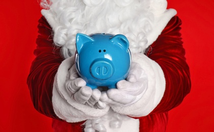 Santa Claus holding piggy bank on red background, closeup