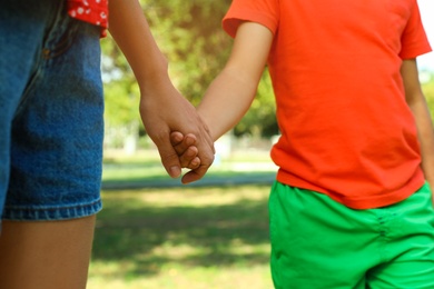 Photo of Little boy and his mother holding hands outdoors, closeup. Family weekend