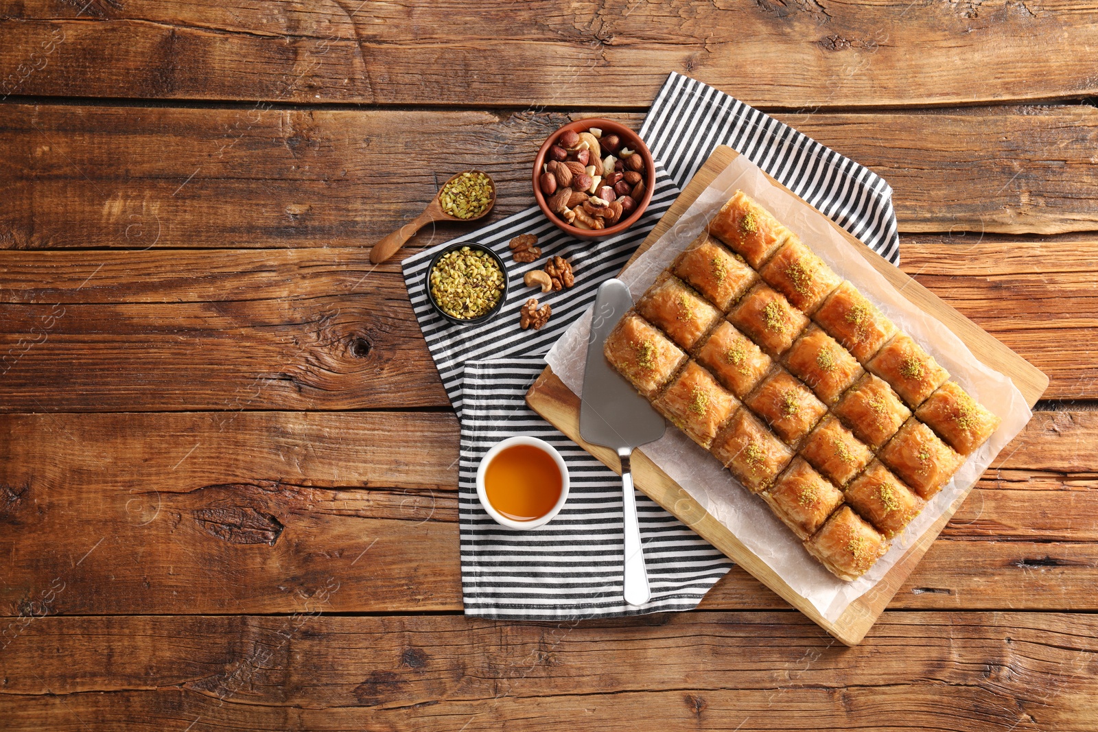 Photo of Delicious sweet baklava, cake server with ingredients on wooden table, flat lay. Space for text