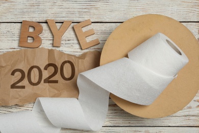 Photo of Flat lay composition with text Bye 2020 and toilet paper on white wooden table, flat lay