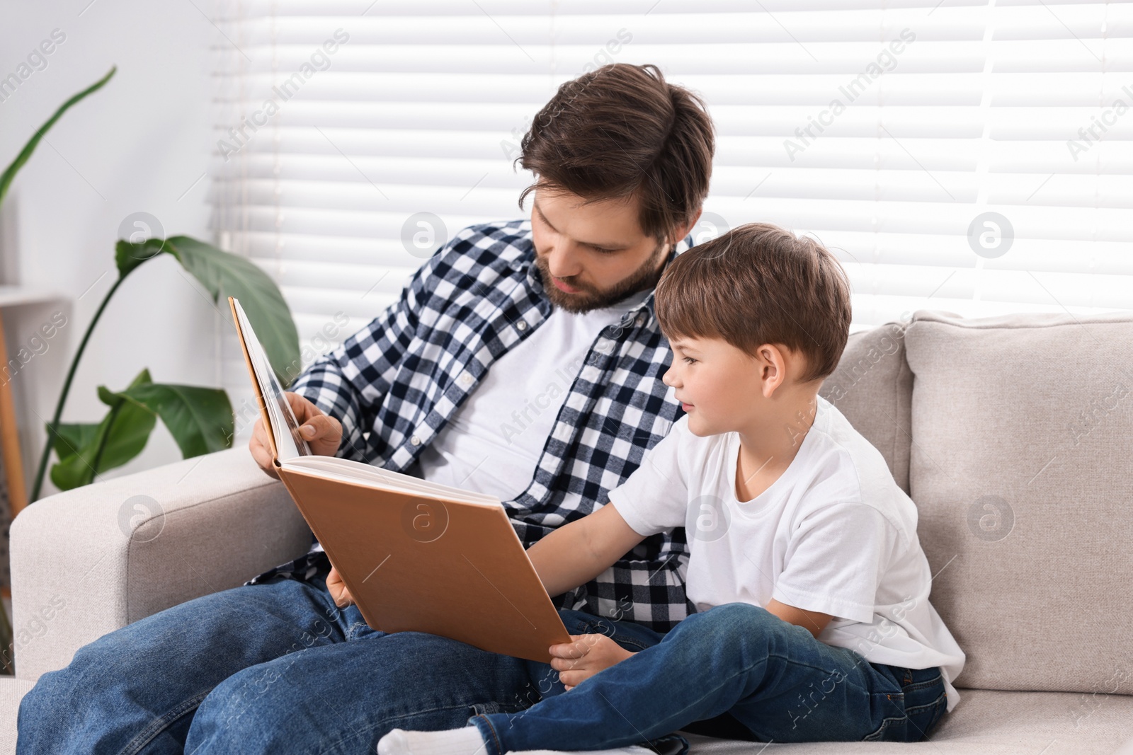 Photo of Dad and son reading book together on sofa at home