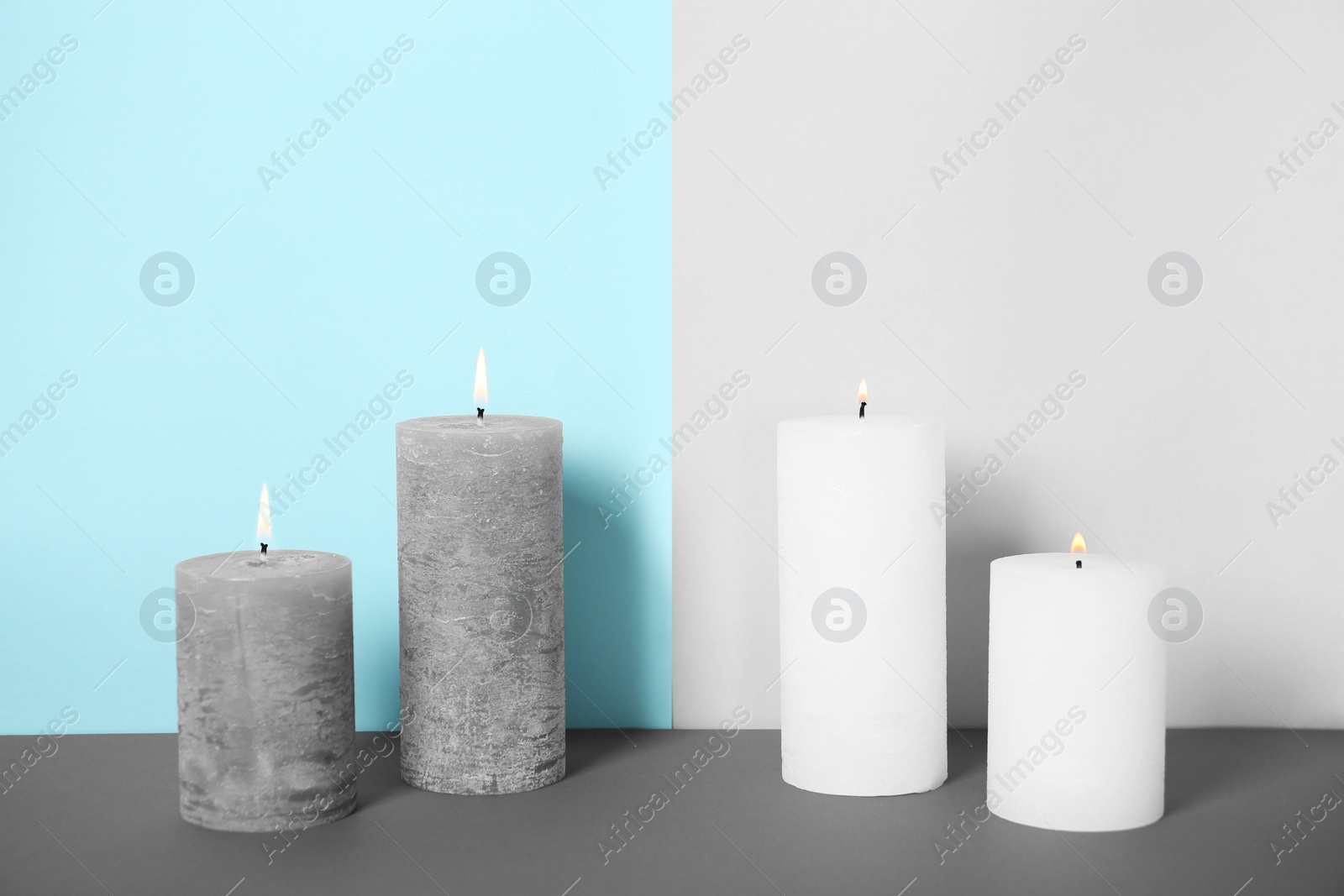 Photo of Decorative wax candles on table against color background