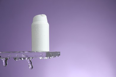 Moisturizing cream in bottle on glass with water drops against violet background. Space for text