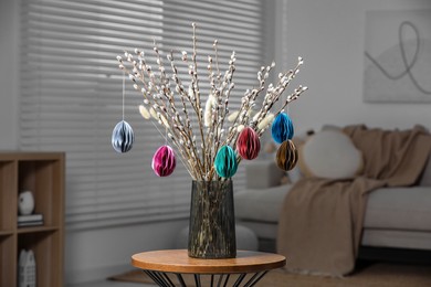 Photo of Beautiful pussy willow branches with paper eggs in vase on wooden table at home. Easter decor