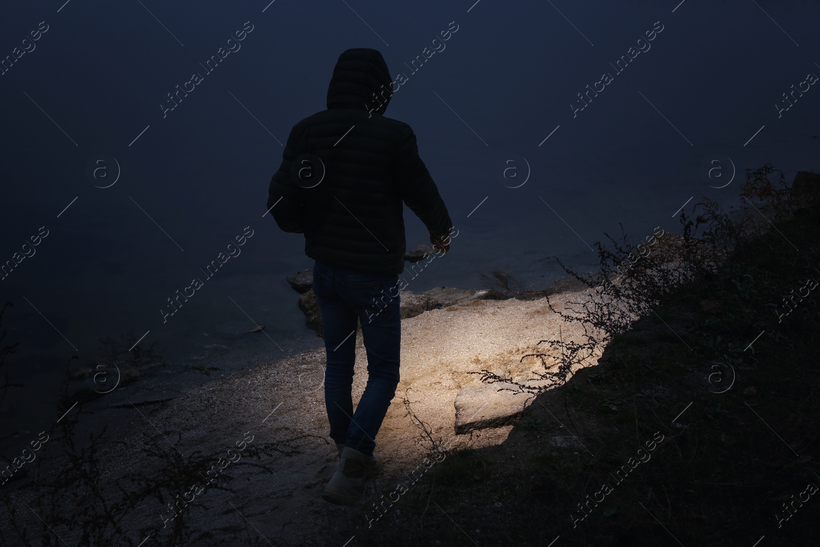 Photo of Man with flashlight walking near river in evening