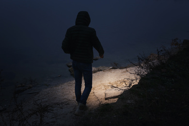 Man with flashlight walking near river in evening