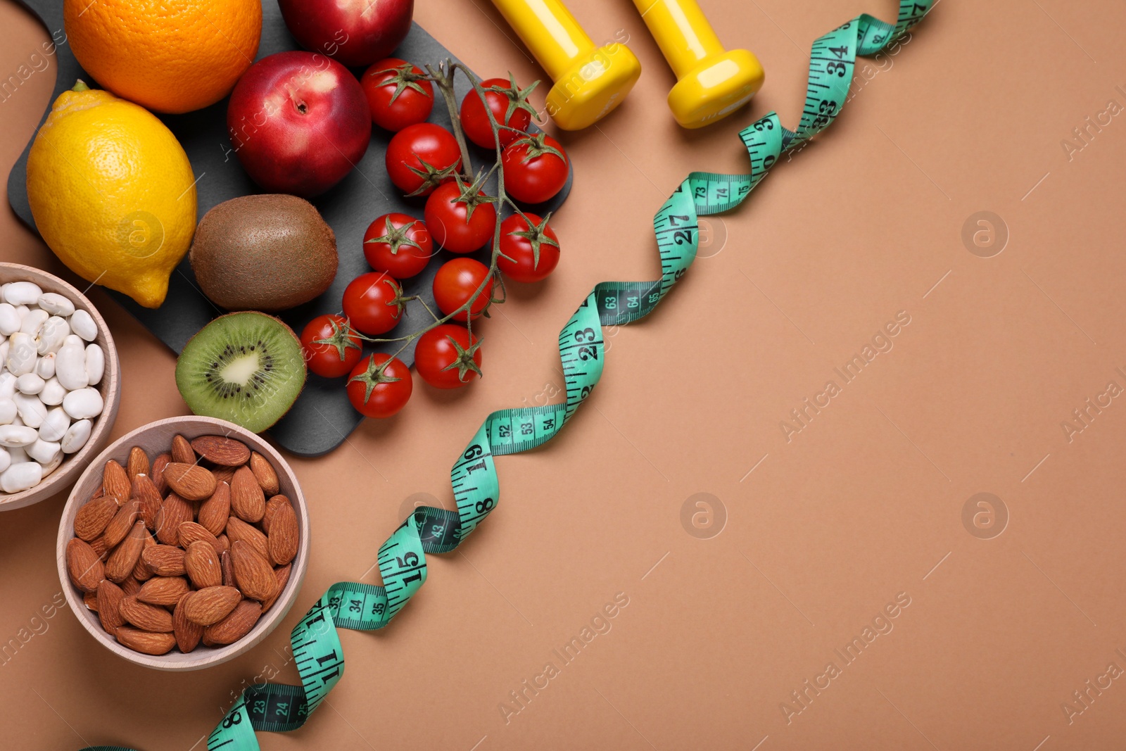 Photo of Measuring tape, almonds, fresh fruits and tomatoes on light brown background, flat lay with space for text. Low glycemic index diet