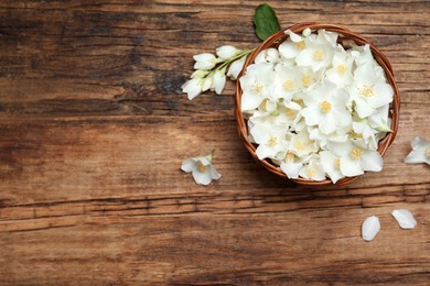 Beautiful jasmine flowers in wicker bowl on wooden table, top view. Space for text