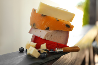Photo of Different types of delicious cheeses and fork on wooden railing outdoors, closeup