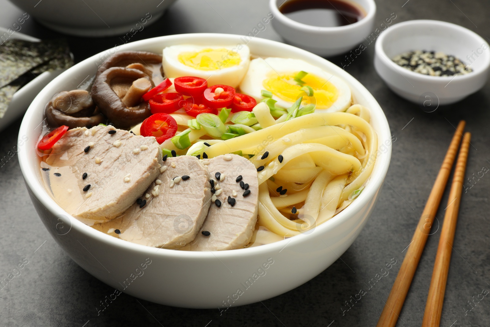 Photo of Delicious ramen with meat in bowl and ingredients on grey textured table, closeup. Noodle soup