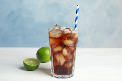Photo of Glass of refreshing soda drink with ice cubes, limes and straw on white wooden table against blue background