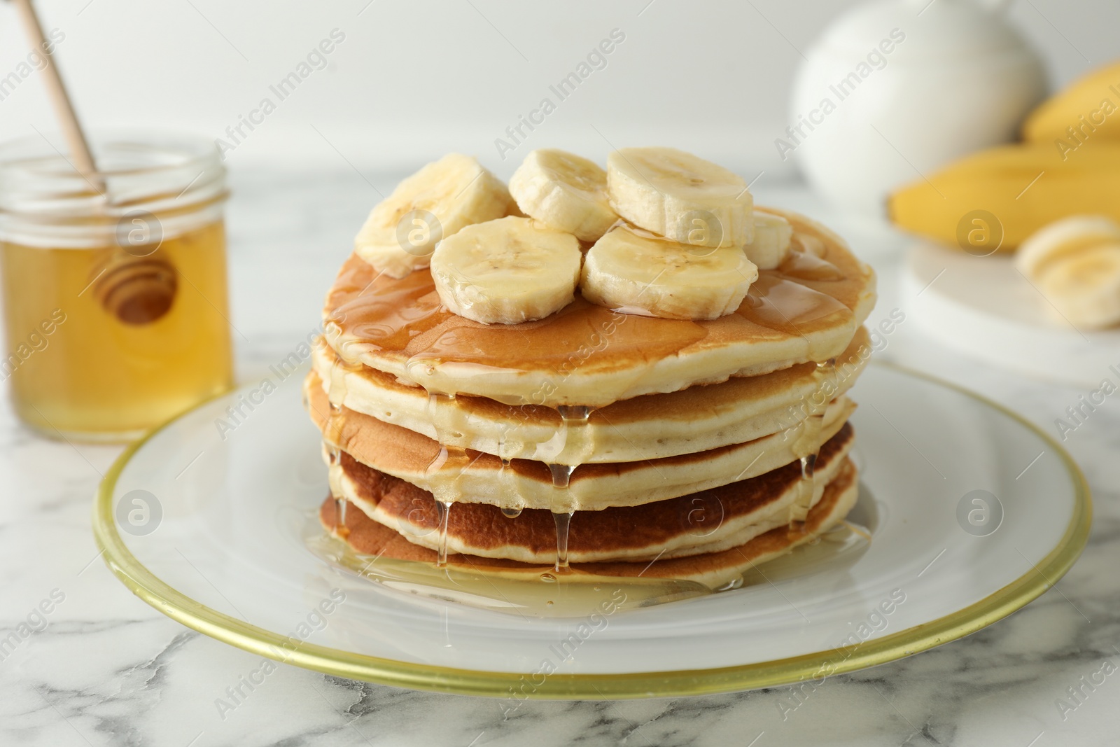 Photo of Delicious pancakes with bananas and honey on white marble table, closeup