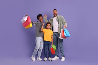 Photo of Family shopping. Happy parents and son with colorful bags on violet background