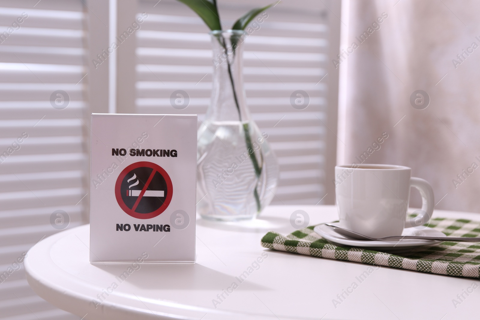Photo of No Smoking No Vaping sign and cup of coffee on white table indoors