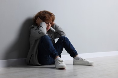 Photo of Child abuse. Upset boy sitting on floor near grey wall