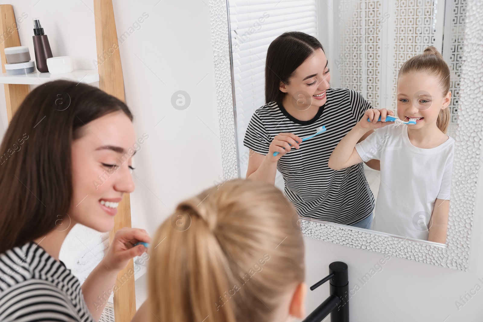 Photo of Mother and her daughter brushing teeth together near mirror in bathroom