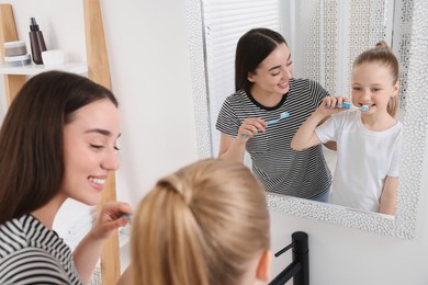 Mother and her daughter brushing teeth together near mirror in bathroom