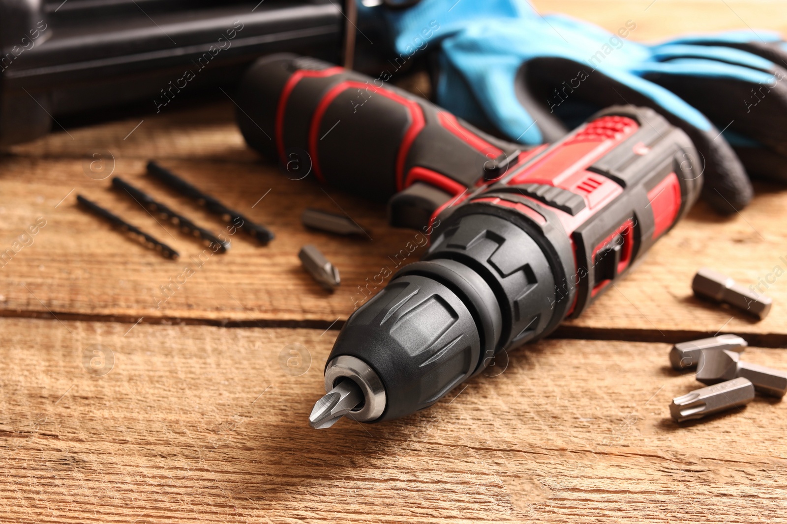 Photo of Electric screwdriver with bits and drills on wooden table, closeup