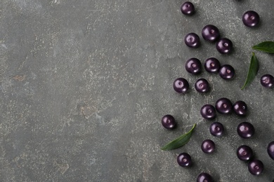 Fresh acai berries and green leaves on grey table, flat lay. Space for text