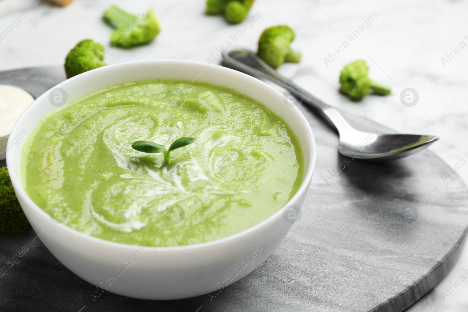 Photo of Bowl of broccoli cream soup served on stone board, closeup