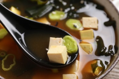 Photo of Delicious miso soup with tofu in spoon above bowl, closeup