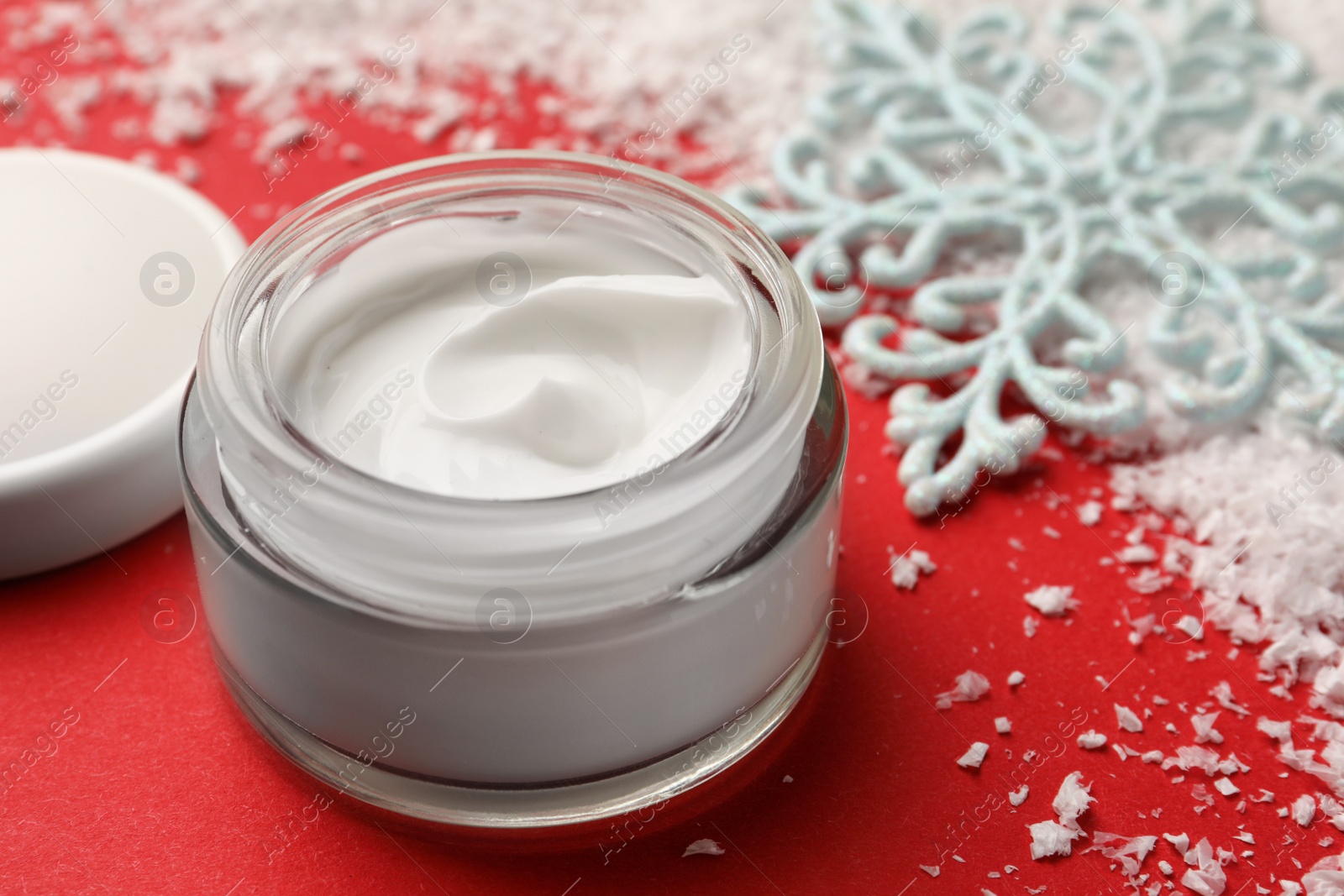 Photo of Winter skin care. Hand cream near decorative snowflake on red background, closeup
