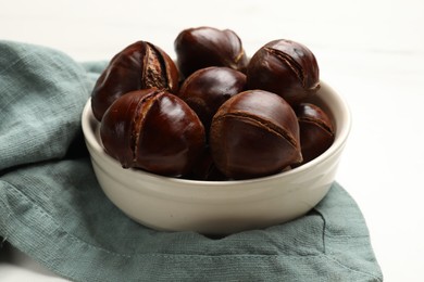 Roasted edible sweet chestnuts in bowl on white table, closeup