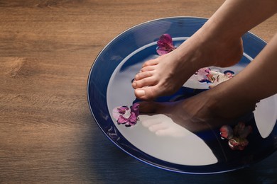 Woman soaking her feet in bowl with water and flowers on wooden floor, closeup with space for text. Spa treatment