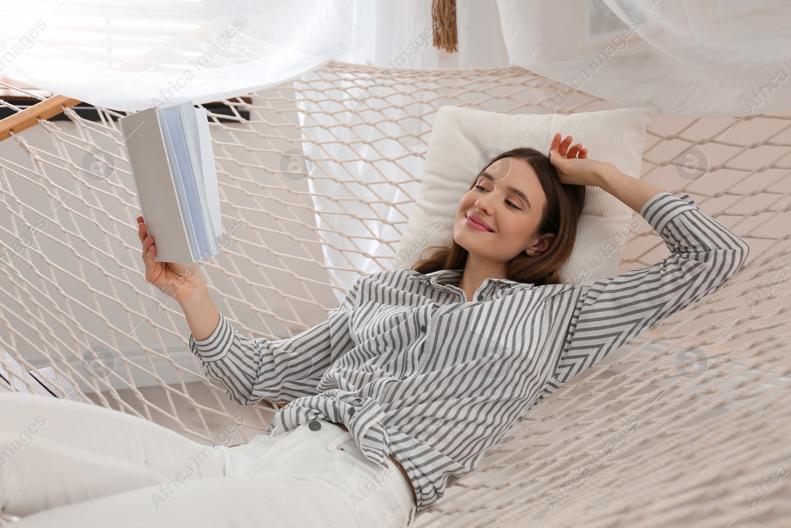 Photo of Happy woman with book in hammock at home