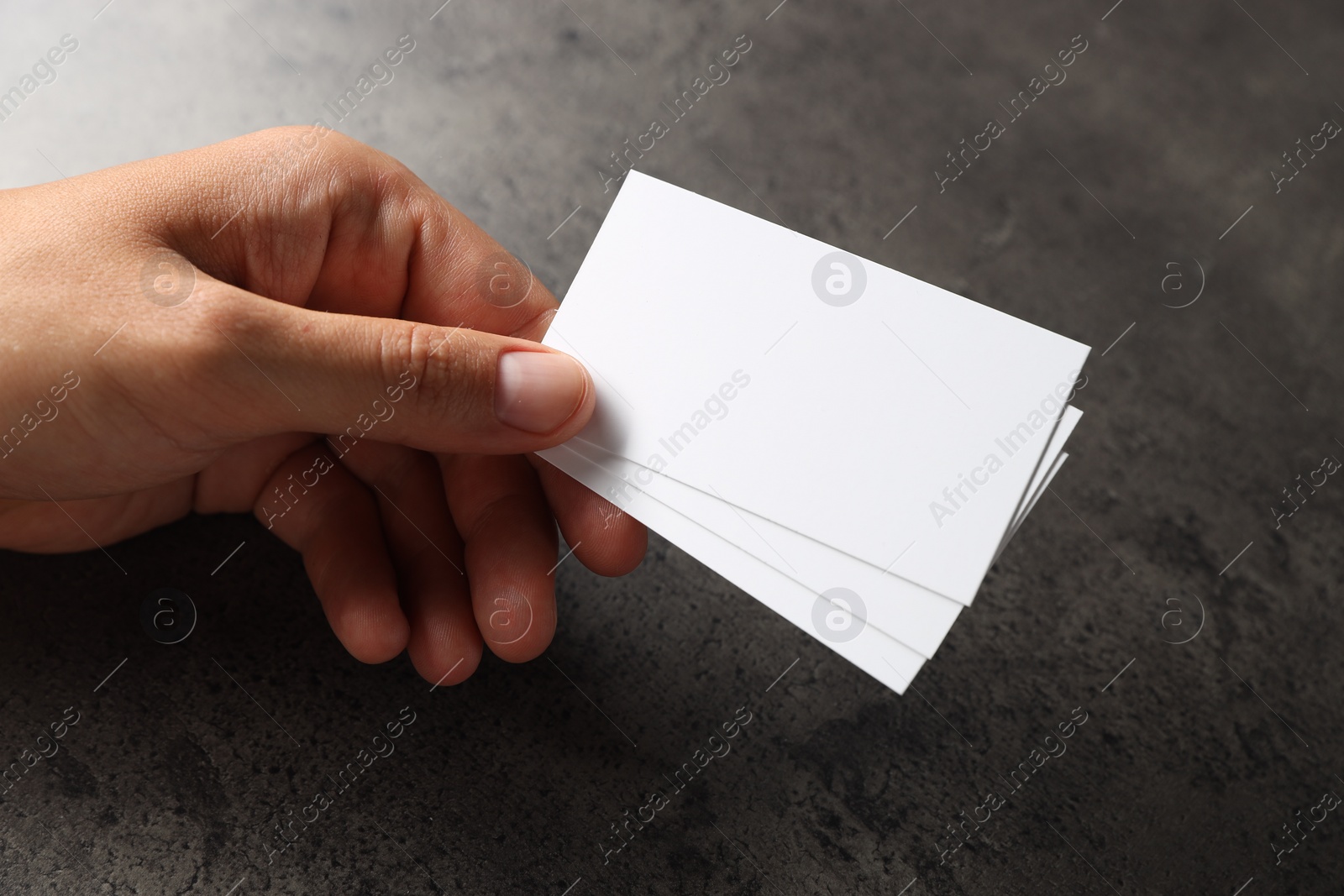 Photo of Man holding blank cards at black textured table, closeup. Mockup for design